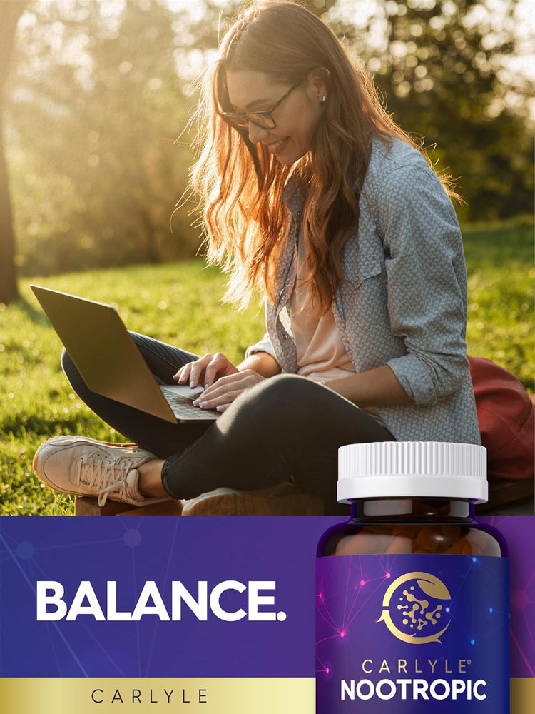A young woman sits on grass, smiling and typing on a laptop, with a Carlyle Nootropic bottle beside her.