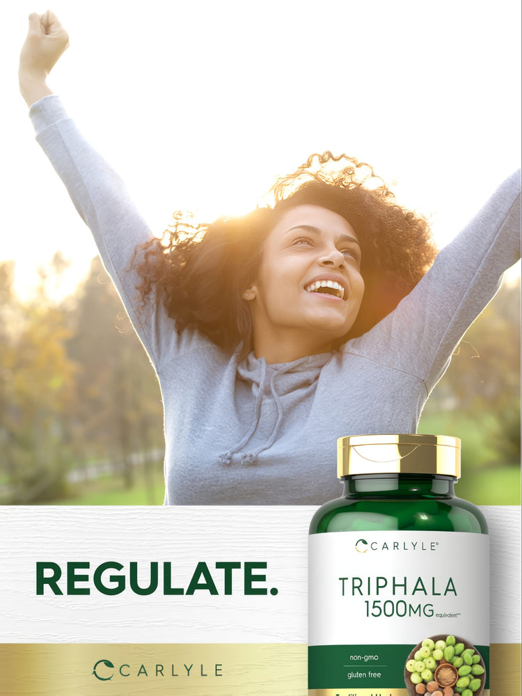 Young adult woman smiling with arms raised outdoors beside a Carlyle Triphala bottle.