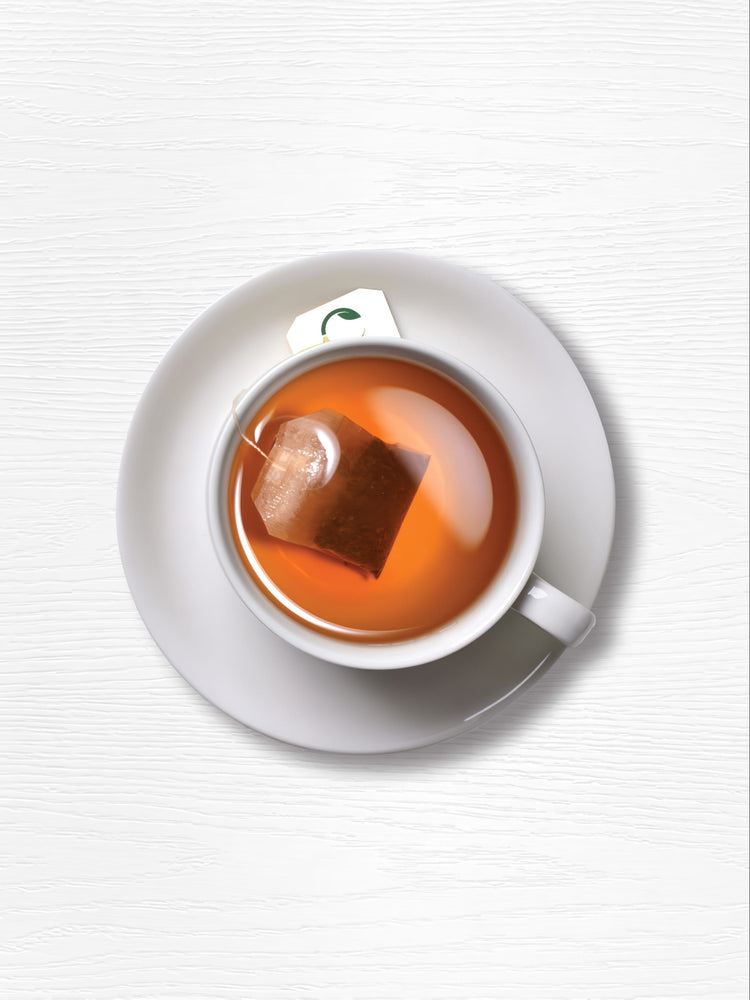 A turmeric tea bag steeps in a white cup on a white saucer.