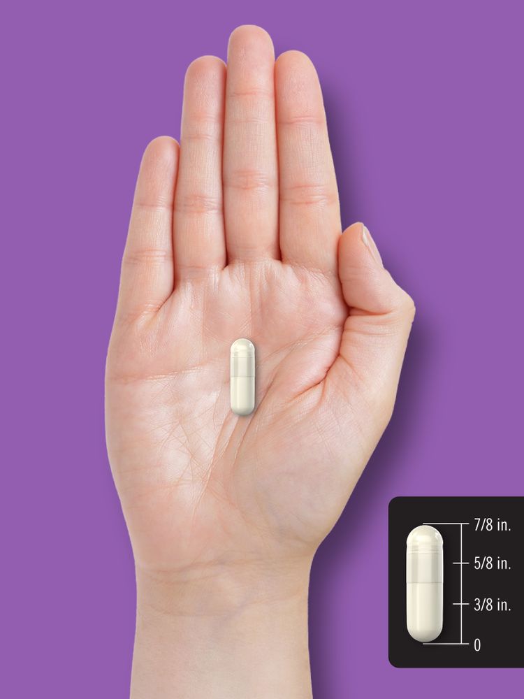 A hand holding an off-white capsule measuring 7/8 inches long on a bulk scale.