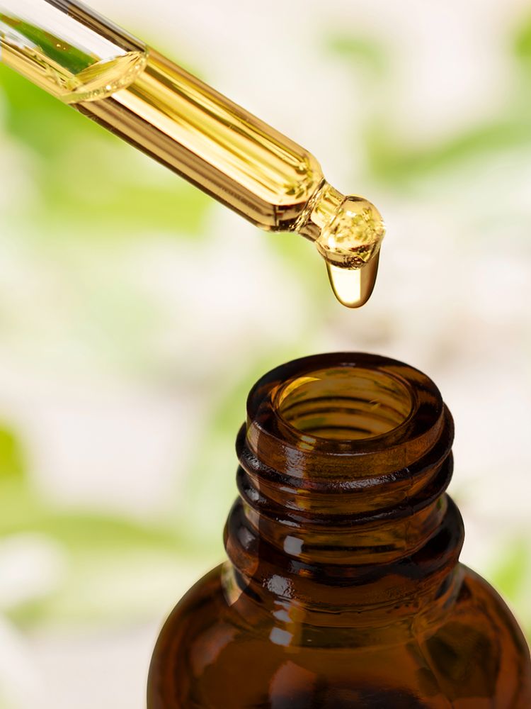 A glass dropper releases a golden liquid into an open amber bottle, highlighting precision and care in dispensing.