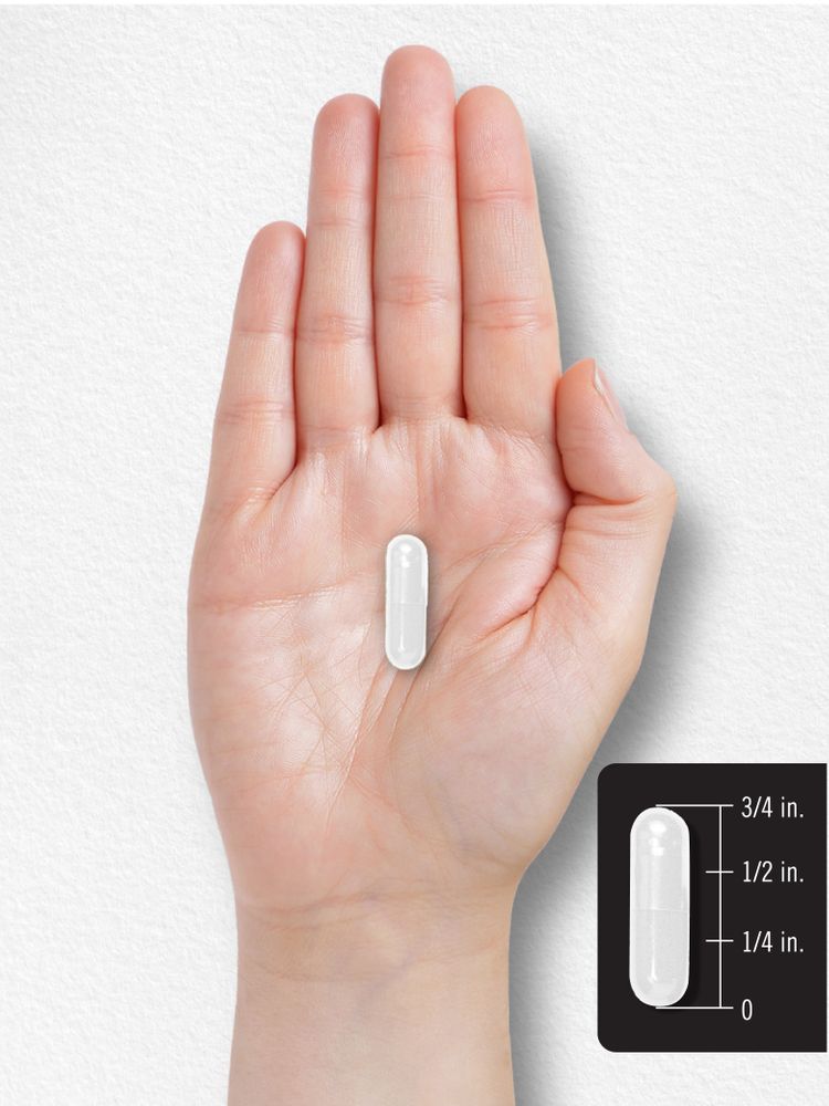 A white capsule sits on a hand scale, measuring 3/4 inch in length and used for supplement purposes.