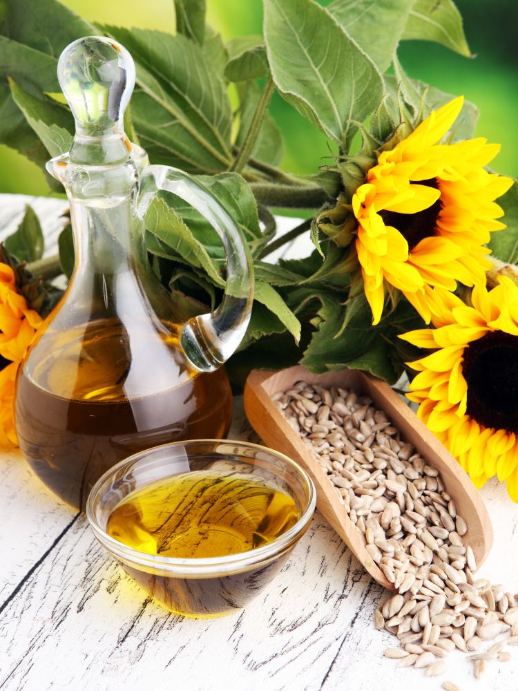 Sunflower Lecithin Liquid in a glass pitcher and bowl, with shelled sunflower seeds in a wooden scoop and whole sunflowers.