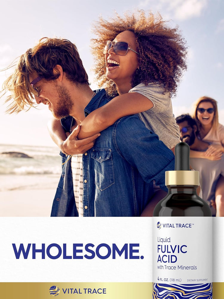 Two young adult couples laugh and piggyback on a beach, holding a Fulvic Acid bottle.