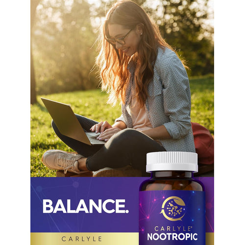 View 6 A young woman sits on grass, smiling and typing on a laptop, with a Carlyle Nootropic bottle beside her.