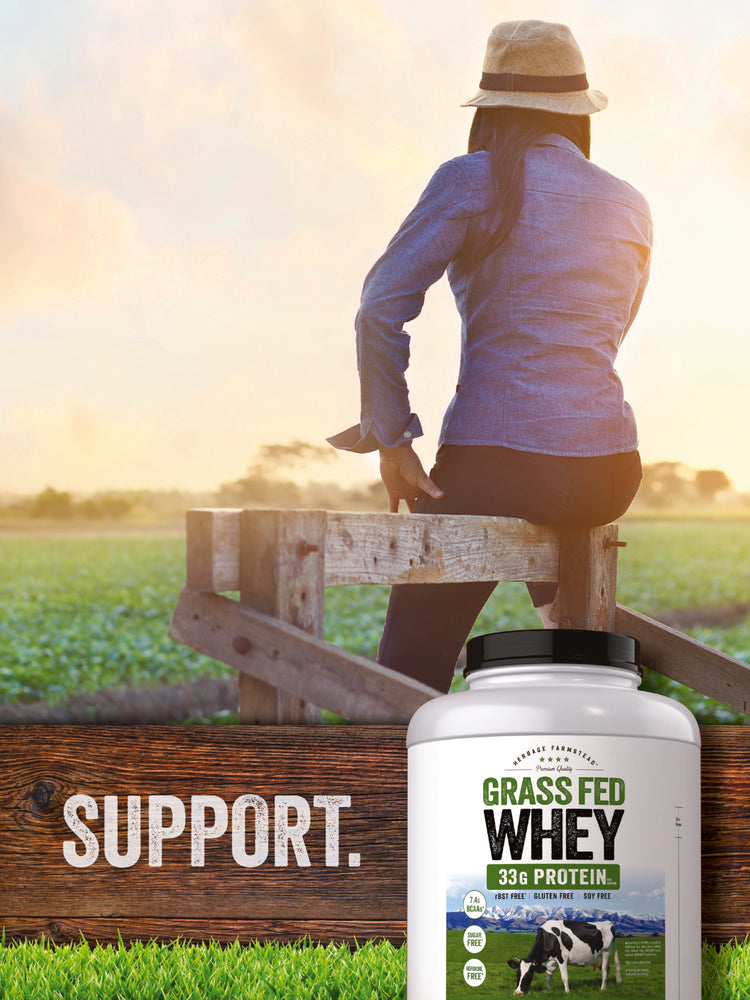A person in a jacket and hat sits on a wooden fence next to a bottle of Carlyle Grass Fed Whey.