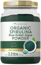 Carlyle Organic Spirulina Blue-Green Algae Powder in a 2.2 lbs (1000 g) jar, shown on a hand scale.