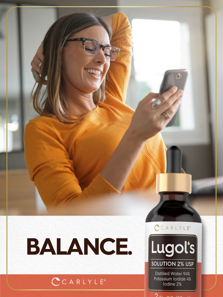 A young adult woman smiles at her phone while holding a bottle of Lugol's Iodine.