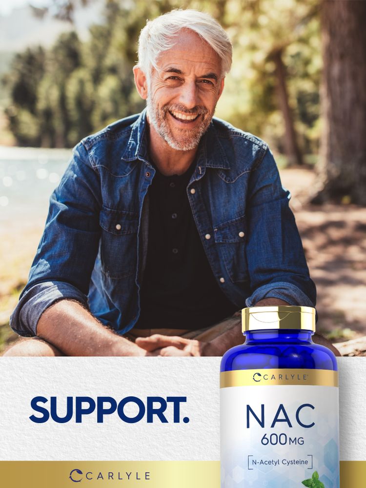 An older man smiling while sitting outdoors with a Carlyle NAC bottle beside him.