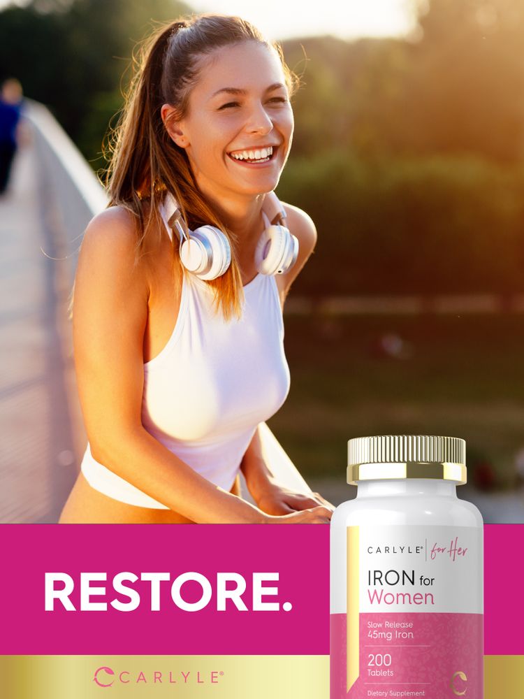 A young woman smiles outdoors wearing headphones, standing next to a Carlyle Iron for Women bottle.