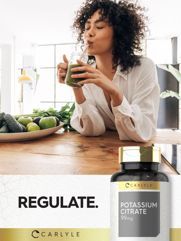 Young woman drinking a green smoothie with fresh produce and a Carlyle Potassium Citrate bottle nearby.