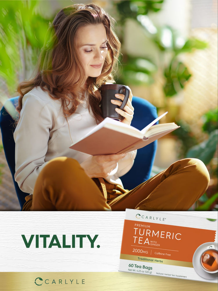 A woman reads a book and drinks from a mug next to a box of Carlyle Turmeric Tea.