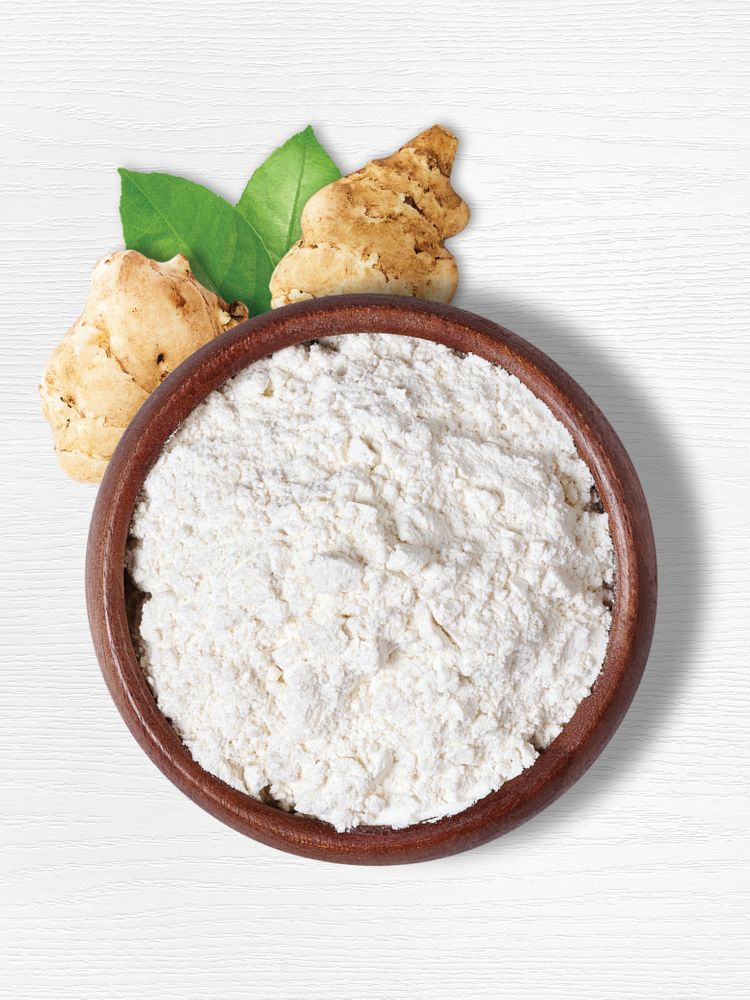 A wooden bowl filled with inulin powder, with two Jerusalem artichoke tubers and green leaves in the background.