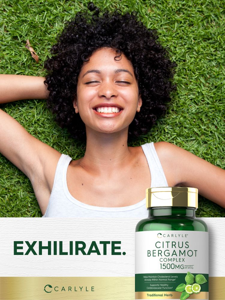 A young woman smiles while lying on grass with eyes closed next to a Carlyle Citrus Bergamot Complex bottle.