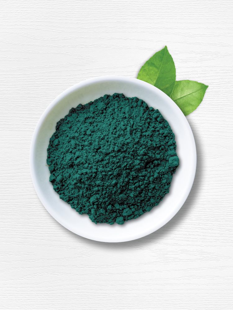 A white bowl contains 2.2 lbs of green Spirulina organic powder, accompanied by two green leaves.
