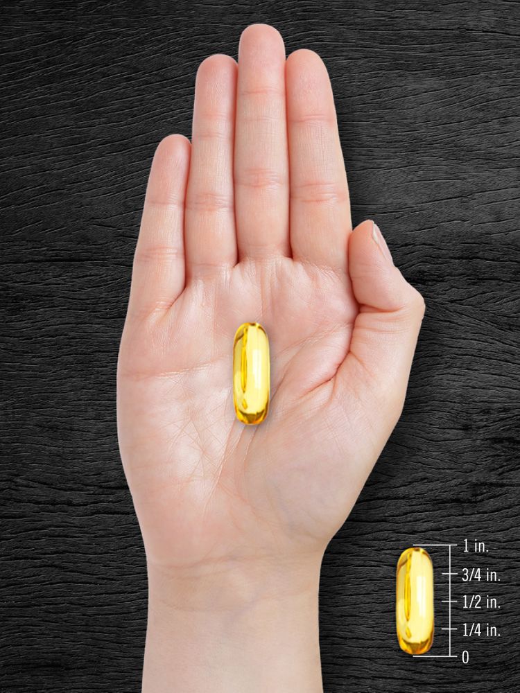 A yellow softgel measuring 1 inch long, displayed on a hand scale.