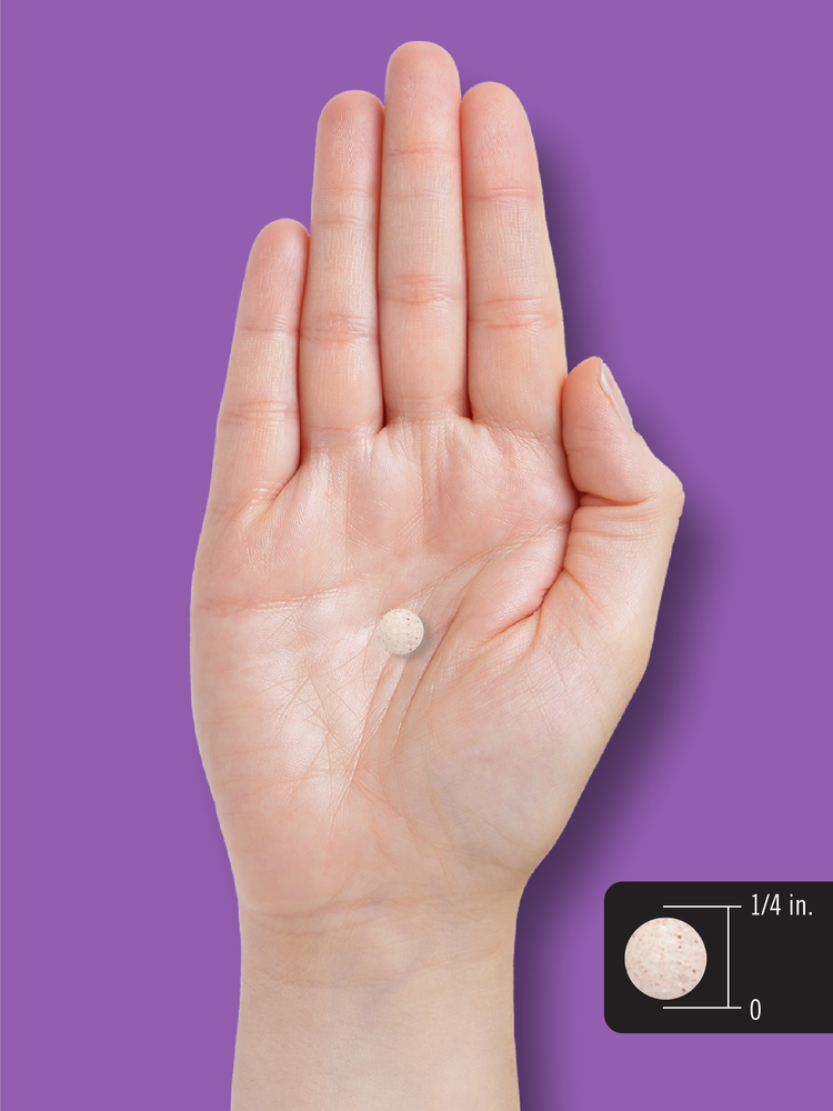 A round tablet with a 1/4 inch diameter, shown on a hand scale for size reference.