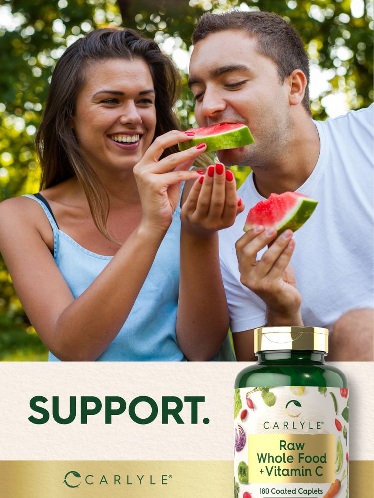 A young man and woman eat watermelon outdoors beside a Carlyle Raw Whole Food + Vitamin C 180 Coated Caplets bottle.
