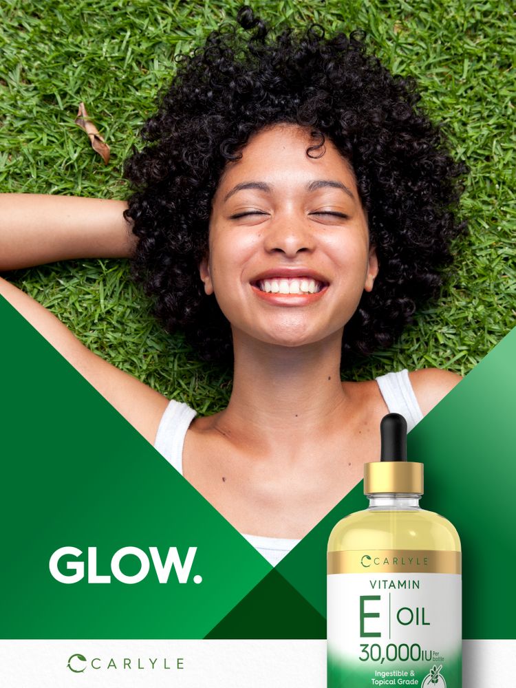 A young woman lies on green grass, smiling with closed eyes, next to Carlyle Vitamin E Oil.