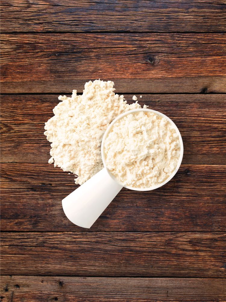 Whey protein powder in a scoop and scattered on a wooden surface.