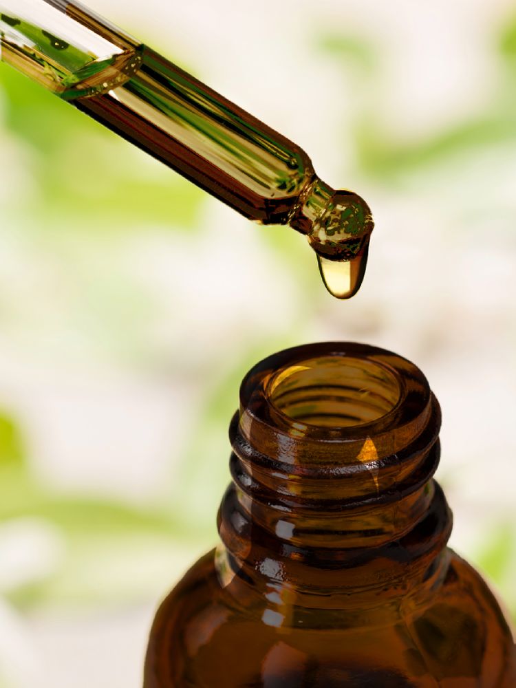 Liquid vitamin C drops from a glass dropper into a brown bottle.