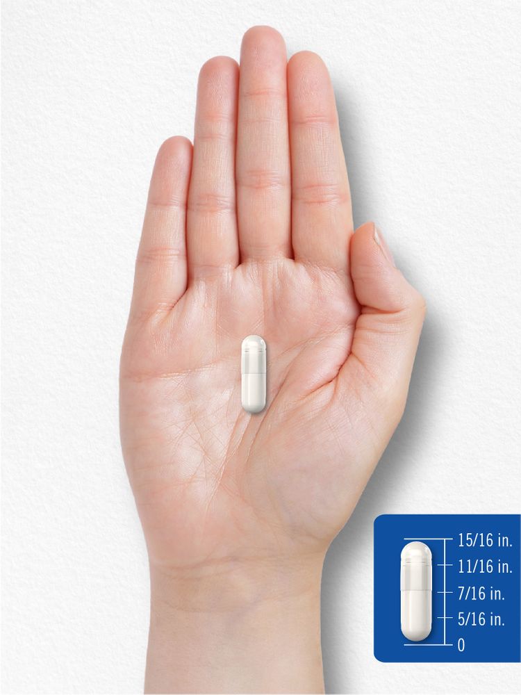 A 15/16 inch white capsule rests on a person's hand.